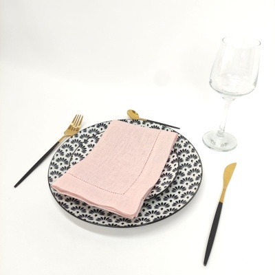 Prato decorado preto e branco com guardanapo rosa, talheres dourados e copo de vinho