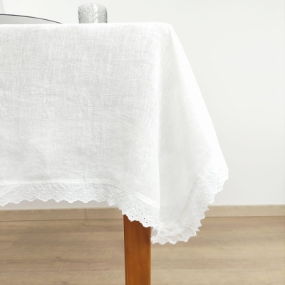 Toalha de mesa branca de linho com bordado nas bordas numa mesa de madeira