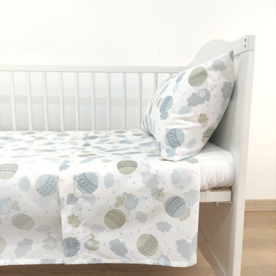 Roupa de cama infantil com padrão de balões e nuvens numa cama branca