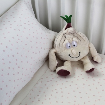 Pelúcia em forma de alho com rosto sorridente sobre roupa de cama branca com padrão vermelho