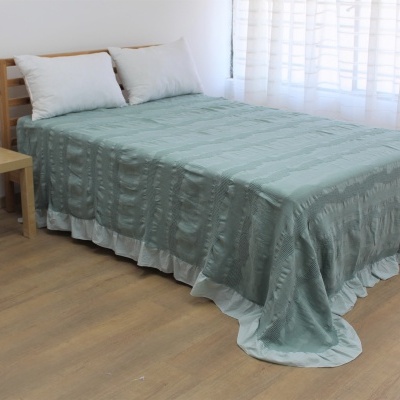 Cama com colcha verde-água texturizada e duas almofadas brancas em quarto com chão de madeira