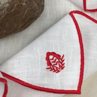 Guardanapo branco com borda vermelha e bordado vermelho ao lado de pão escuro