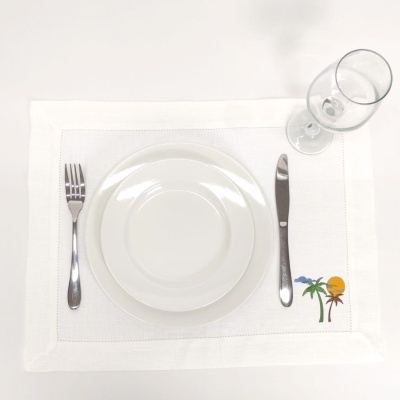 Individual de mesa branco com bordado colorido, pratos brancos, talheres e copo