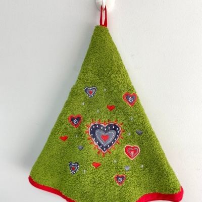 Toalha de cozinha verde com bordado de corações pendurada numa parede branca