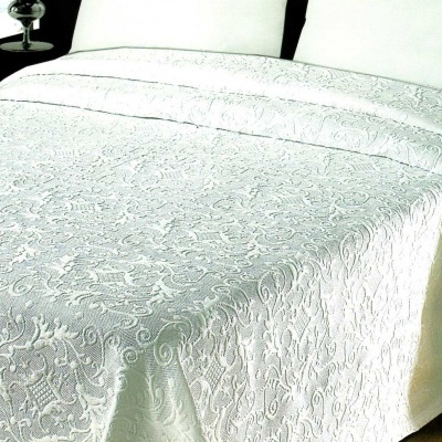 Colcha branca com padrão floral em relevo sobre cama com almofadas brancas