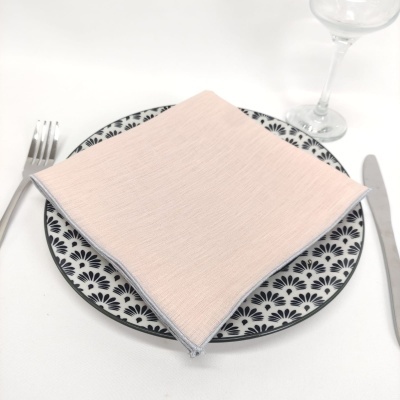 Mesa posta com prato de cerâmica com padrão preto, guardanapo rosa claro, talheres e copo de vidro