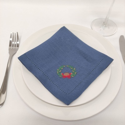 Guardanapo azul com bordado em prato branco, talheres de metal e copo de vidro