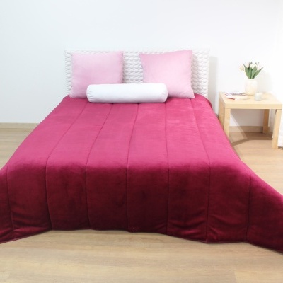 Cama com edredão vinho e almofadas rosa com mesa de apoio e plantas ao lado