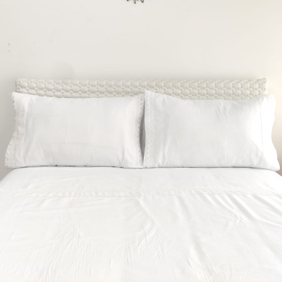 Cama com almofadas e lençol brancos com cabeceira trançada