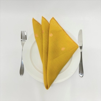 Conjunto de mesa com garfo, faca, prato branco e guardanapos amarelos com padrões cor-de-rosa.