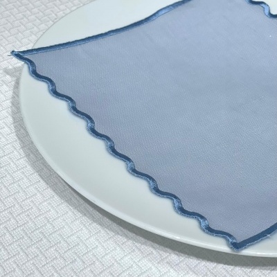 Guardanapo azul com borda ondulada sobre prato branco em toalha de mesa clara