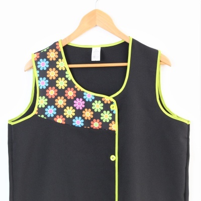 Colete preto com padrão de flores coloridas e bordas amarelas em cabide