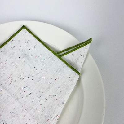Guardanapo branco com pontos coloridos e borda verde sobre prato branco