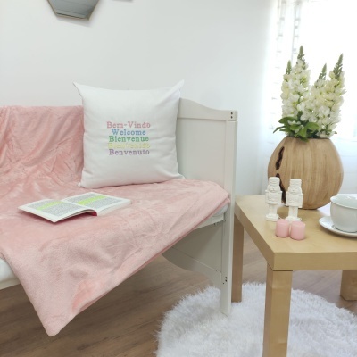 Sofá branco com manta e almofada colorida ao lado de mesa com velas e flores, em ambiente luminoso.