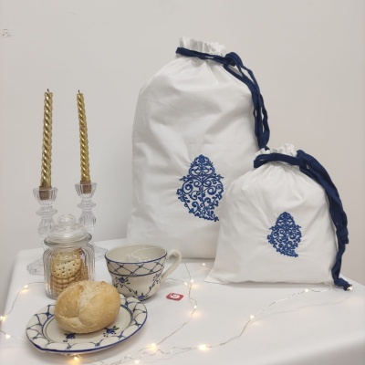 sacos de pano brancos com estampas azuis, vela dourada, frasco de vidro com bolachas, chávena e prato azuis com pão