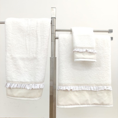 Conjunto de toalhas de banho brancas com detalhes em riscas creme e folhos, penduradas numa estrutura metálica