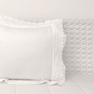 Travesseiro branco com fronha bordada e colcha branca em cama com cabeceira acolchoada