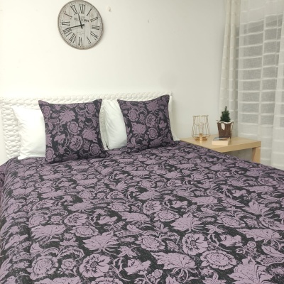 cama com colcha e fronhas florais rosa e preto, relógio com números romanos e mesa de cabeceira com planta