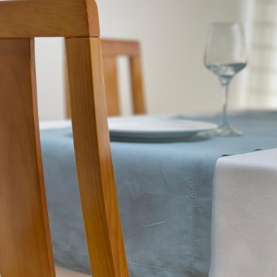 Cadeira de madeira junto a mesa com toalha branca e caminho de mesa azul claro com prato e copo