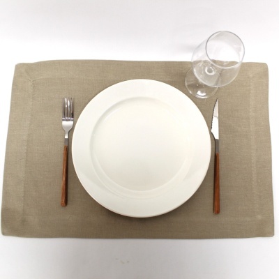 Conjunto de mesa com prato branco, garfo, faca com cabo de madeira e taça sobre placemat bege.