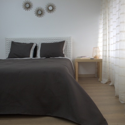 Quarto com cama de cabeceira branca rendada e roupa de cama cinza escuro