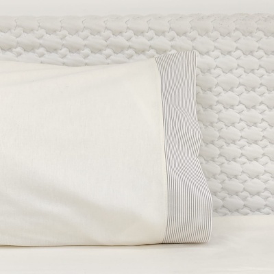 Travesseiro branco com franja riscada cinza e branco numa cama com colcha branca acolchoada