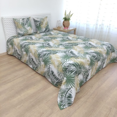 Cama com edredão e almofadas decorativas com padrão de folhas verdes e bege num quarto com piso em madeira clara.