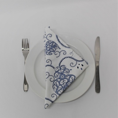 Guardanapo branco com padrão azul sobre prato branco, garfo e faca ao lado
