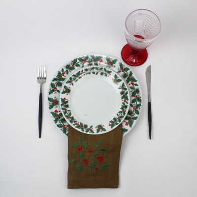 Mesa posta com pratos decorados, talheres, guardanapo bordado e copo vermelho