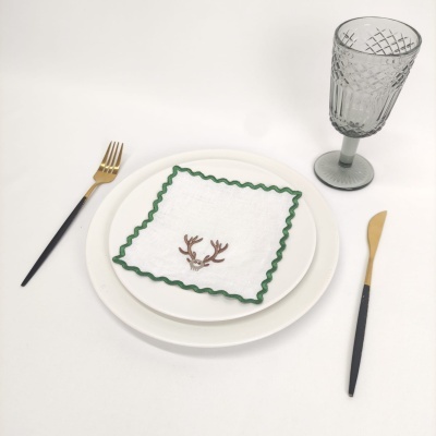 Conjunto de jantar com pratos brancos, guardanapo bordado, talheres preto e dourado, e copo cinza