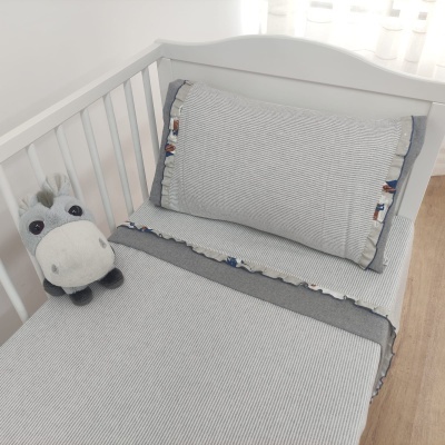 Berço branco com roupa de cama cinza e branca com padrão riscas, almofada decorativa e peluche
