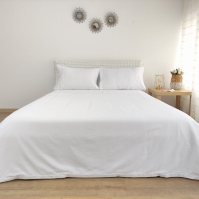 Cama de casal com roupa de cama branca e cabeceira trançada, decorada com espelhos e mesa com flores.