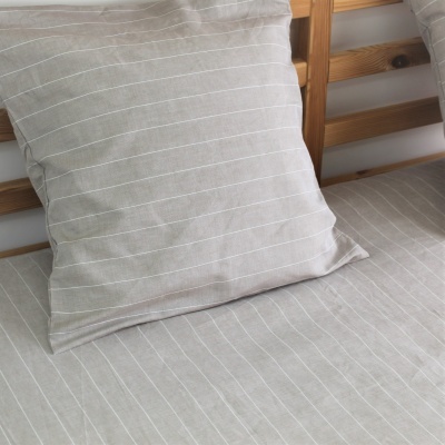 Almofada e capa de edredão bege com riscas brancas sobre cama de madeira