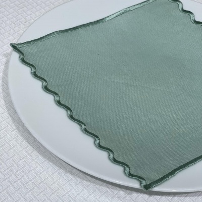 Guardanapo verde com borda ondulada sobre prato branco em toalha branca