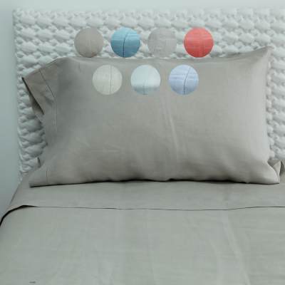 Almofada cinzenta esverdeada com lençol da mesma cor em cama com cabeceira branca texturizada