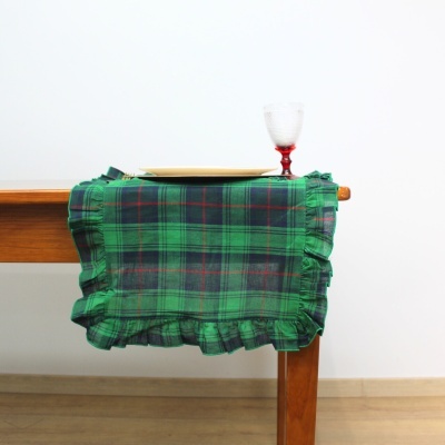 Toalha xadrez verde com borda franzida numa mesa de madeira com prato e copo.