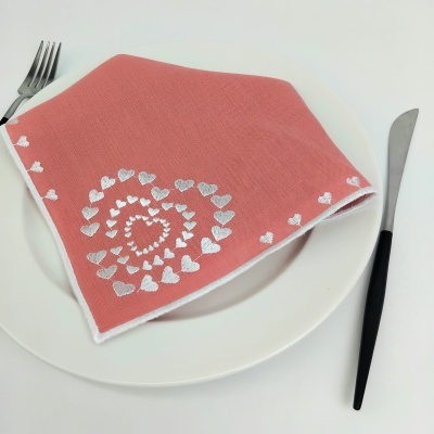 Guardanapo cor de rosa com corações brancos em espiral sobre prato branco, com garfo e faca ao lado