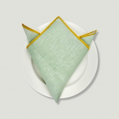 Guardanapo verde claro com borda amarela em prato branco