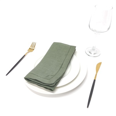 Talheres pretos e dourados com prato branco, guardanapo verde e copo de vidro