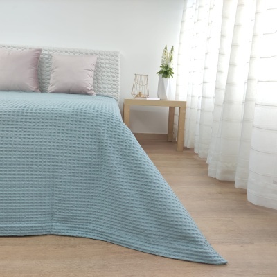 Cama com cobertura azul claro e almofadas rosa em quarto moderno com mesa e vaso branco.