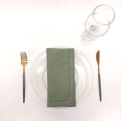 prato branco com guardanapo verde, talheres com detalhes dourados e copo de vidro transparente