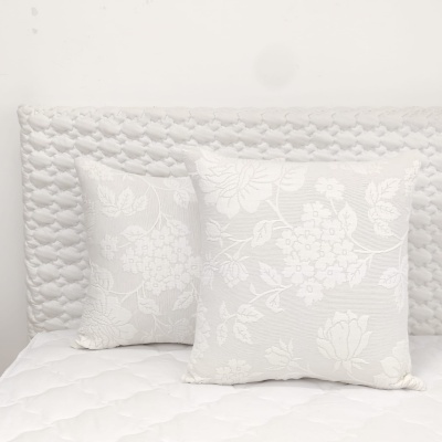 Três almofadas brancas decorativas com padrão floral sobre cama branca matelassê