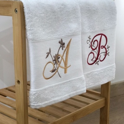 duas toalhas de banho brancas com bordados de letras A e B penduradas numa estrutura de madeira