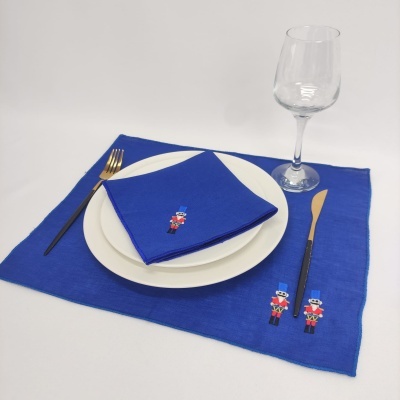 Jogo americano e guardanapo azuis com bordado de soldadinhos, prato branco, talheres dourados e copo de vidro.