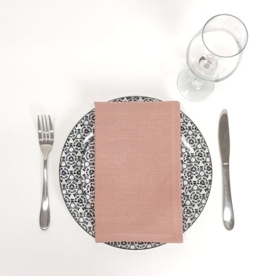 Mesa posta com prato branco e preto, guardanapo rosa, garfo, faca e copo de vinho.