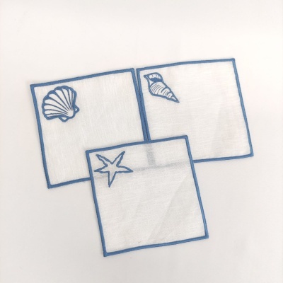Três guardanapos brancos com bordas azuis e bordados de conchas marinhas