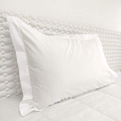 Almofada branca com fronha branca lisa sobre cama branca com cabeceira texturizada