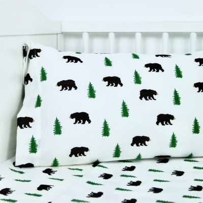 Conjunto de almofada e lençol branco com estampado de ursos e árvores verdes numa cama branca