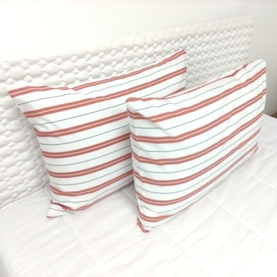 Almofadas com riscas vermelhas e brancas sobre cama com cabeceira acolchoada branca