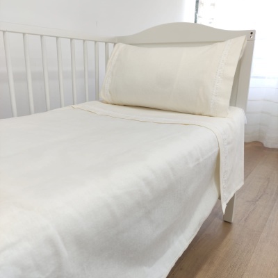 Cama de criança com roupa de cama creme e estrutura branca junto a janela com cortinas brancas
